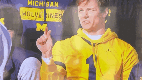 a man wearing a yellow michigan wolverines sweatshirt giving a thumbs up
