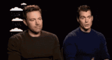 two men are standing next to each other in a dark room and one of them is making a funny face .