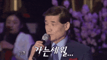 a man in a suit is singing into a microphone with korean writing on it .