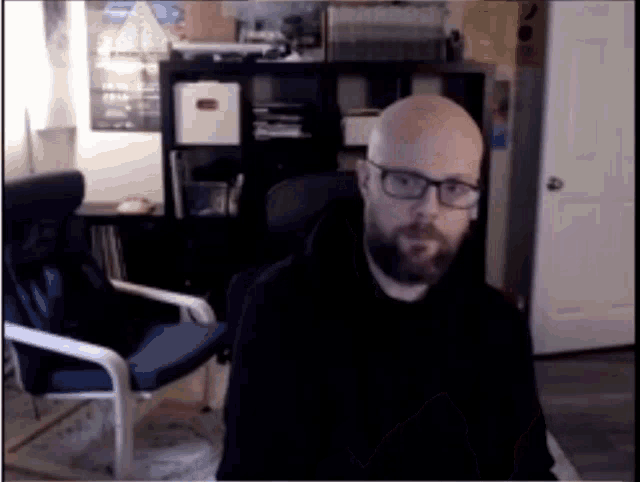 a bald man with glasses is sitting in a chair in a room