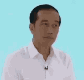 a man in a white shirt with a microphone on his neck is making a funny face with his eyes closed .