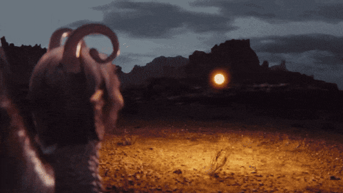 a goat with horns is standing in a field with mountains in the background