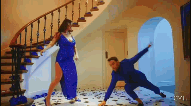 a woman in a blue dress is dancing next to a man in a blue suit on the floor .
