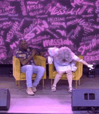 a man and a woman are sitting in front of a wall that has messiah written all over it