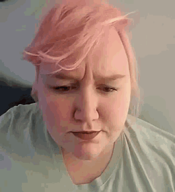 a woman with pink hair and a green shirt is making a sad face .