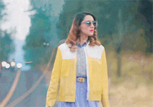 a woman wearing sunglasses and a yellow jacket is walking down the street .