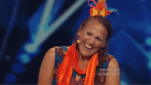 a woman wearing an orange scarf and a colorful hat is laughing on a stage .