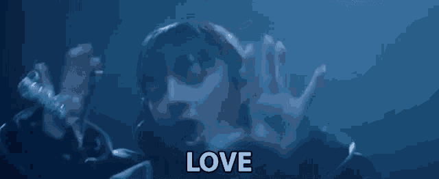 a woman is singing into a microphone in a dark room and the word love is visible in the background .