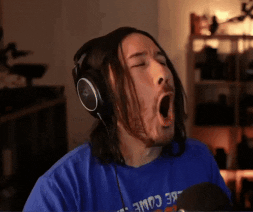 a man wearing headphones and a blue shirt with the word come on it is yawning