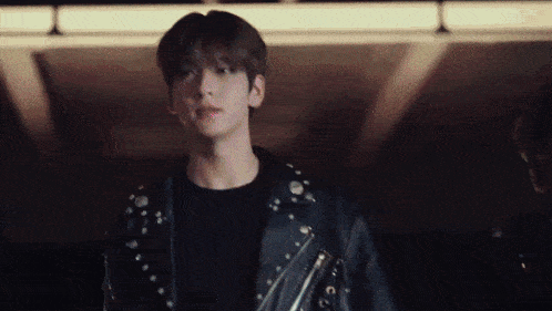 a young man wearing a black leather jacket and a black shirt is walking in a dark room .