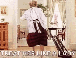 a woman is carrying a suitcase in a living room with the words `` treat her like a lady '' .