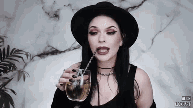 a woman in a black hat is drinking from a glass with a straw