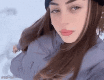 a woman is taking a selfie in the snow while wearing a hat and jacket .