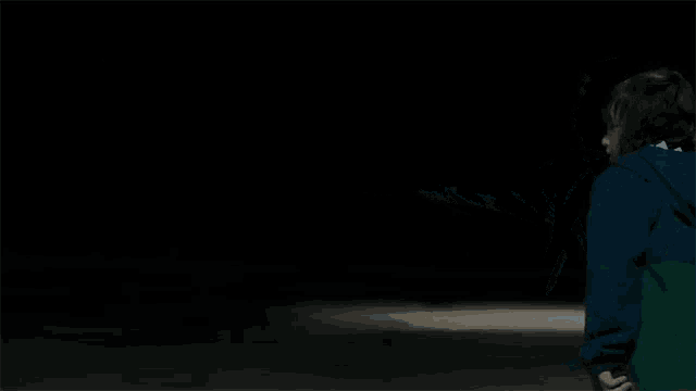 a boy in a blue jacket is holding a hockey stick in the dark .