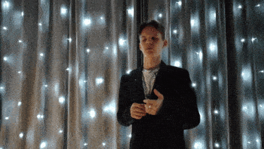 a man in a suit stands in front of a curtain with lights hanging from it