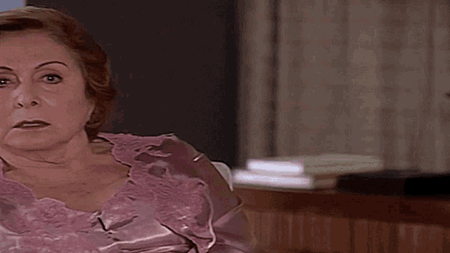 an older woman is sitting on a couch wearing a pink robe