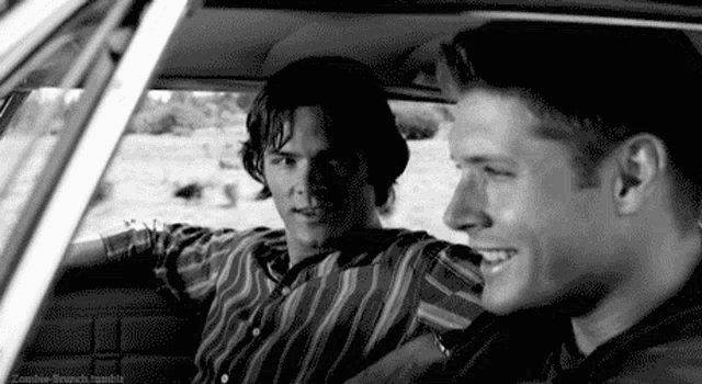 two men are sitting in the back seat of a car .