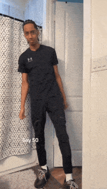 a man wearing a black under armour shirt stands in a bathroom