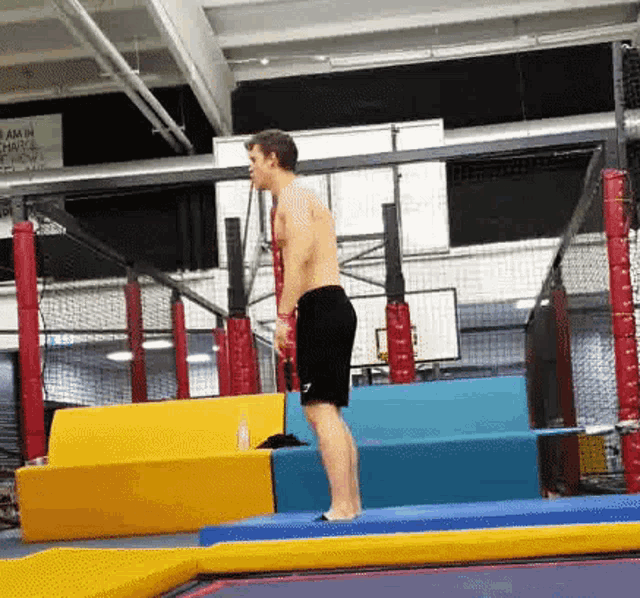 a shirtless man in black shorts is jumping on a trampoline in a gym
