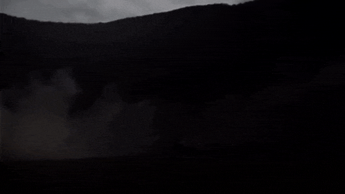 a black and white photo of a mountain at night with a light coming out of it .