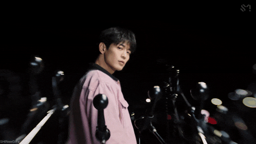 a man in a pink shirt is standing in front of a bunch of microphones