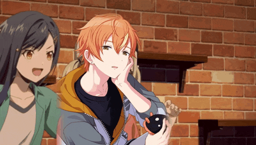 a boy and a girl are standing in front of a brick wall and the boy is holding something in his hand