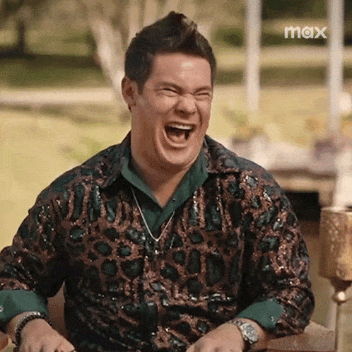 a man in a leopard print shirt is laughing with his mouth open while sitting in a chair .