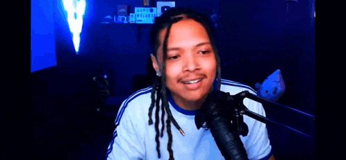 a man with dreadlocks is sitting in front of a microphone with the words diam berhalusinasi above him .