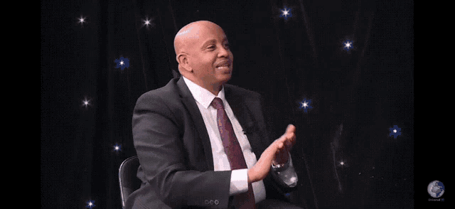 a man in a suit and tie is clapping his hands in front of a black background