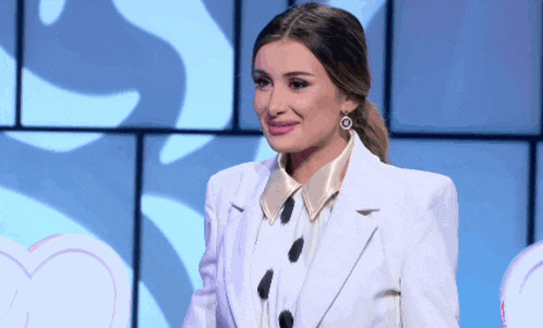 a woman in a white suit and gold earrings smiles