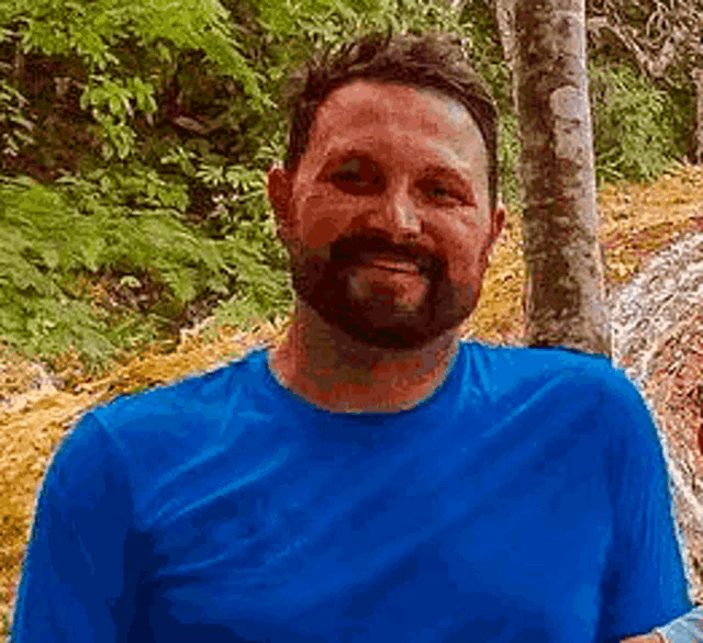 a man with a beard is wearing a blue shirt and smiling for the camera .