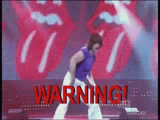 a man in a purple shirt is dancing on a stage in front of a rolling stones sign .