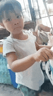 a little boy in a white shirt is standing in front of a bunch of water bottles .
