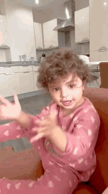 a little girl with curly hair is sitting on a couch in a kitchen .