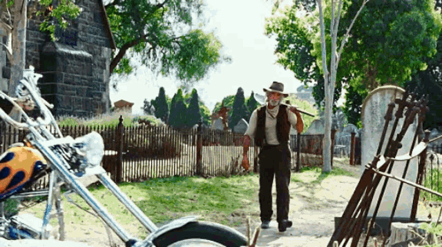 a man in a cowboy hat is standing in front of a cemetery