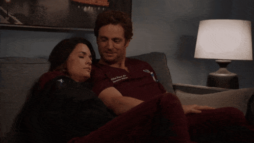 a man and woman are laying on a couch with a lamp in the background