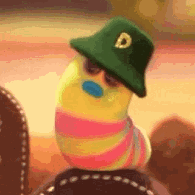 a colorful worm wearing a green hat and sunglasses is sitting on a shoe .