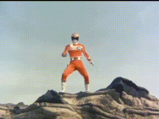 a red power ranger is standing on top of a rocky hill .