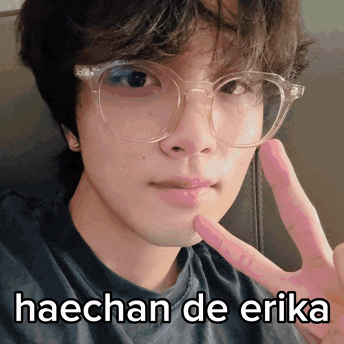 a young man wearing glasses is giving a peace sign and the words haechan de erika are above him