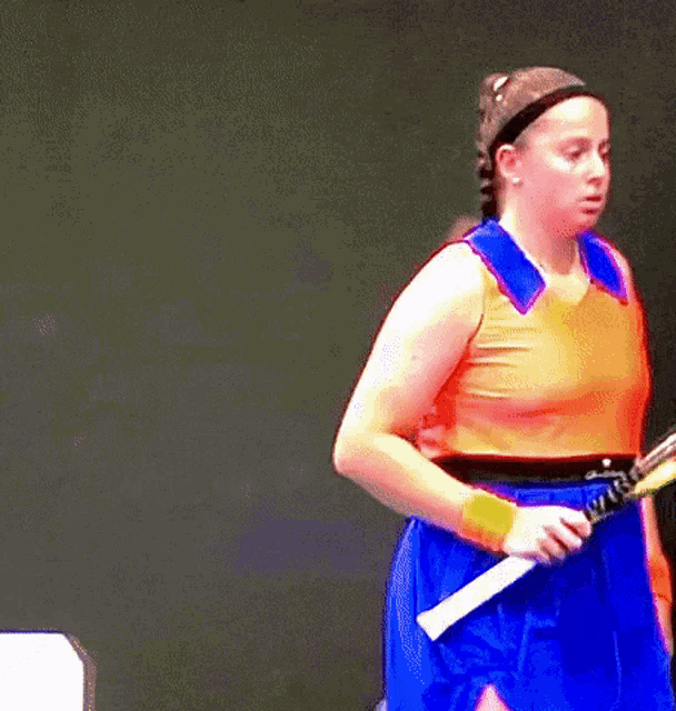 a woman in an orange top and blue skirt is holding a tennis racket .