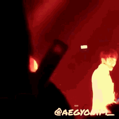 a group of people are standing in a dark room with a red light behind them and the words @aegyonim on the bottom