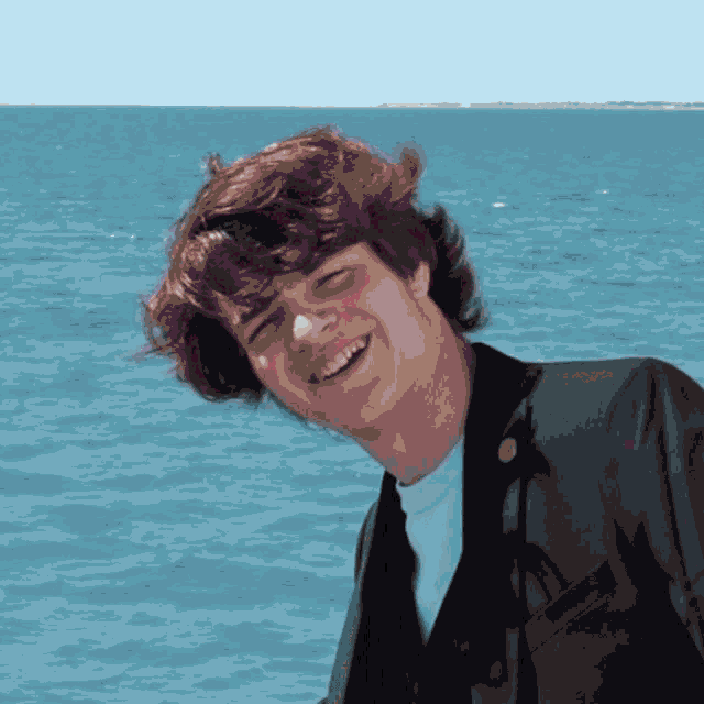 a young man stands in front of the ocean smiling