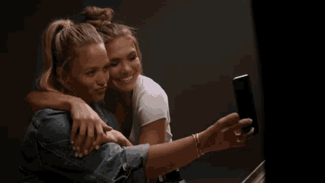 two women are hugging and taking a selfie with a cell phone
