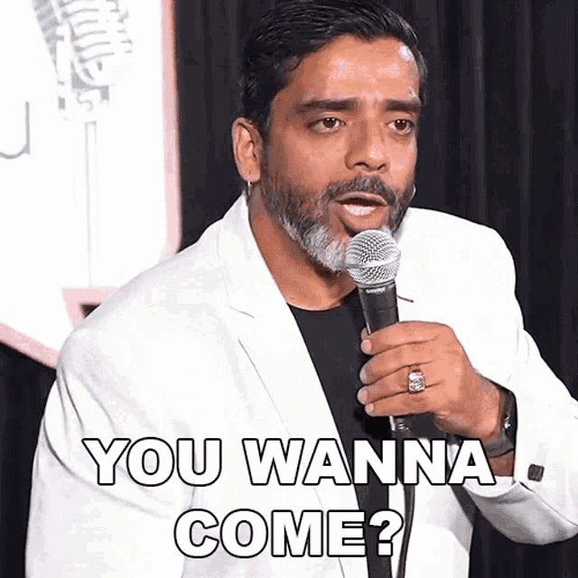 a man in a white suit is holding a microphone and saying you wanna come