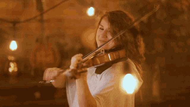 a woman in a white shirt is playing a violin in a dark room