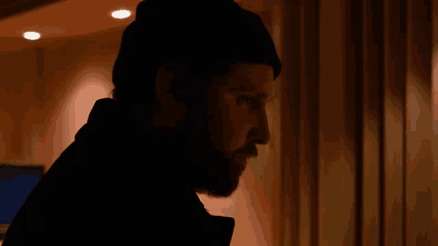 a man with a beard wearing a black hat is standing in a dark room