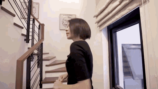 a woman is walking down a set of stairs next to a window with a poster on the wall that says la nationale
