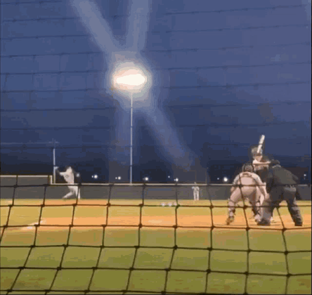 a baseball game is being played in the dark with a light shining through the fence