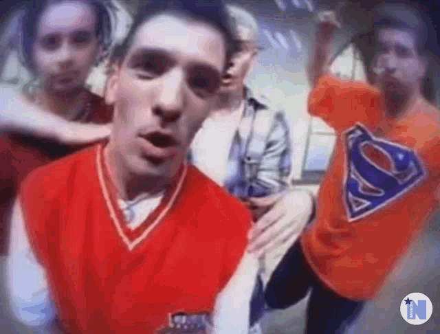 a group of people are standing next to each other and one of them is wearing an orange superman shirt .