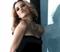 a woman in a black dress is standing in front of a window and making a funny face .